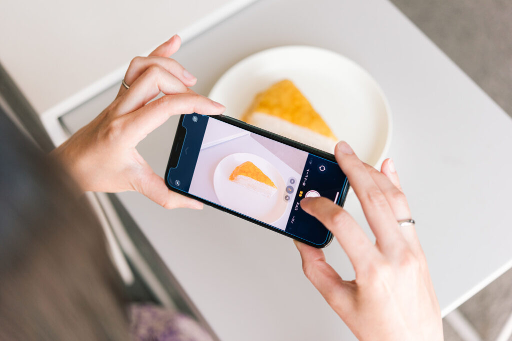 白いお皿に盛ったケーキを、スマホで真上から撮影している手元