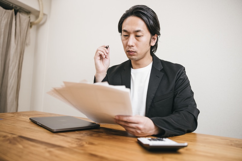 ノートパソコンと電卓を前に、書類を見ながら自分の事業に合う集客方法を考える人