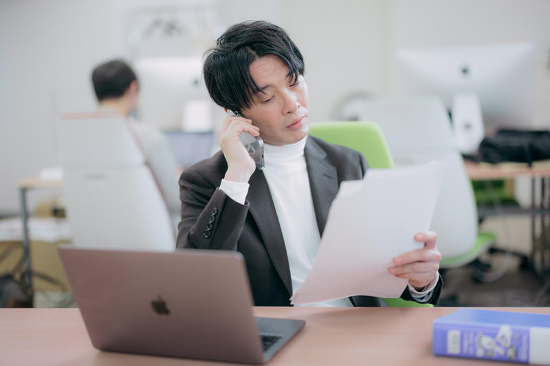 メモを確認しながら電話で相談している男性。エラーが出たときは慌てて触らず、状況をまとめて制作会社に連絡する様子