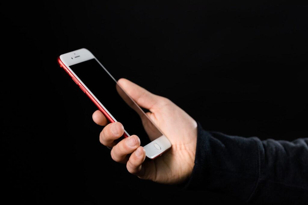 赤いスマートフォンを手に持つ様子。自分のお店の情報がどう表示されるか、手元で確かめるイメージ